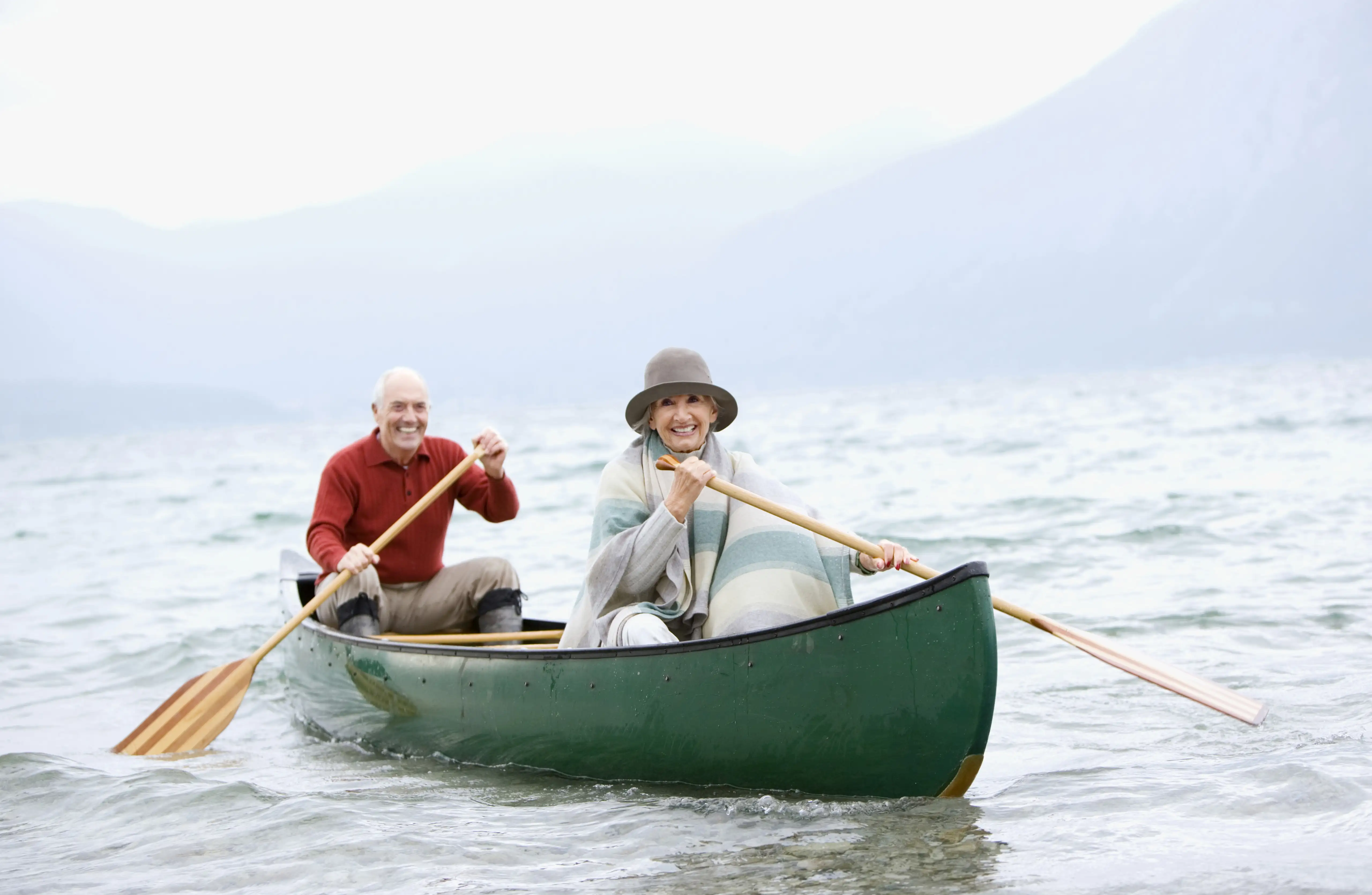 Älteres Paar in einem Boot auf einem grauen See. Beide halten ein Paddel in der Hand.