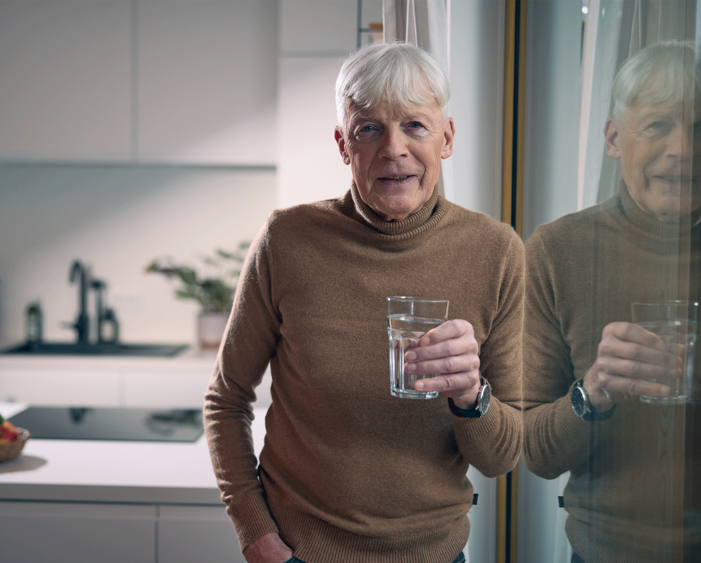 Ein älterer Herr hält ein Glas mit Wasser und einem Präparat in der Hand, das ihm hilft, die Beschwerden einer vergrößerten Prostata zu lindern