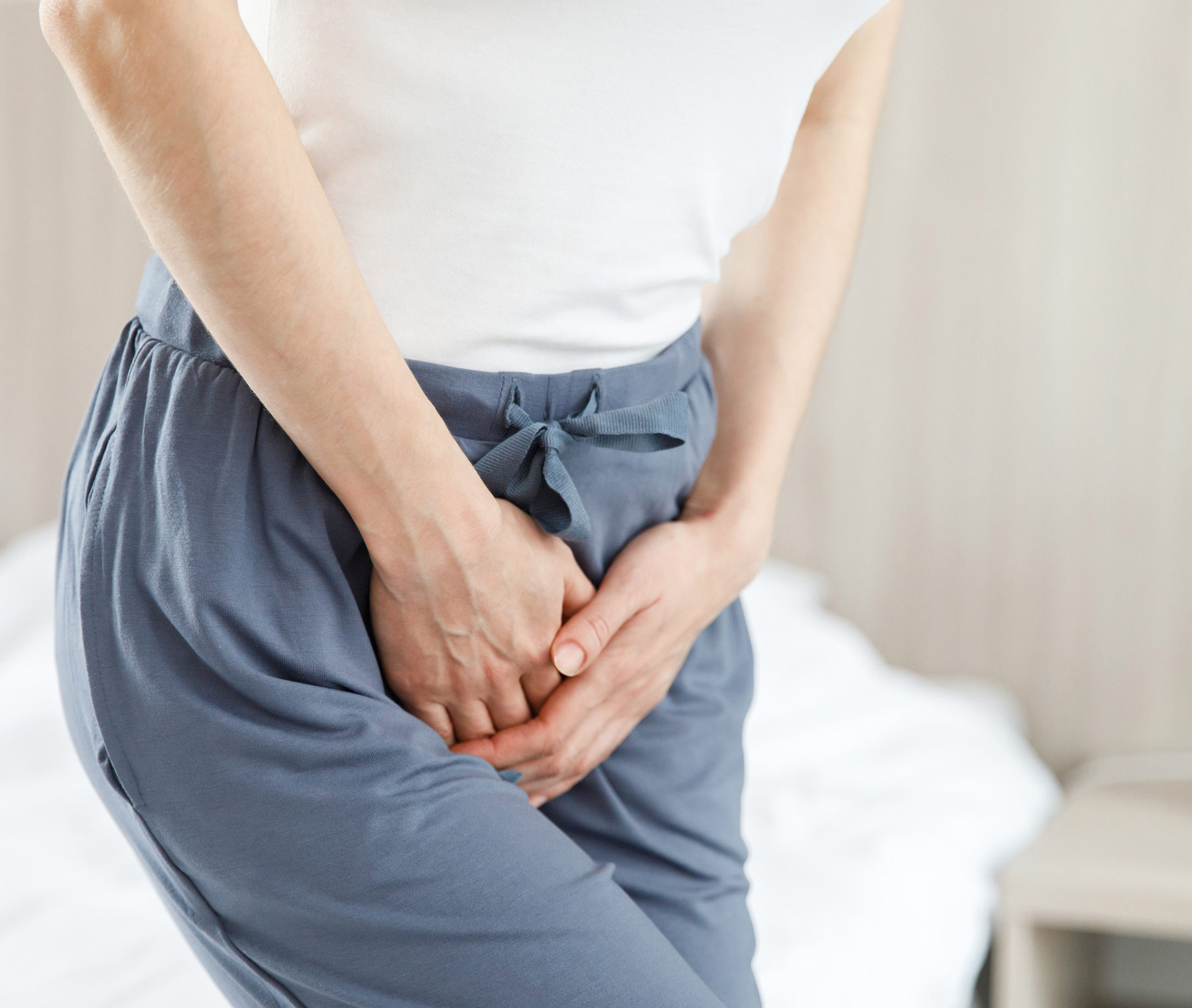 Frau mit Blasenentzündung hält sich die Hände vor den Schritt.