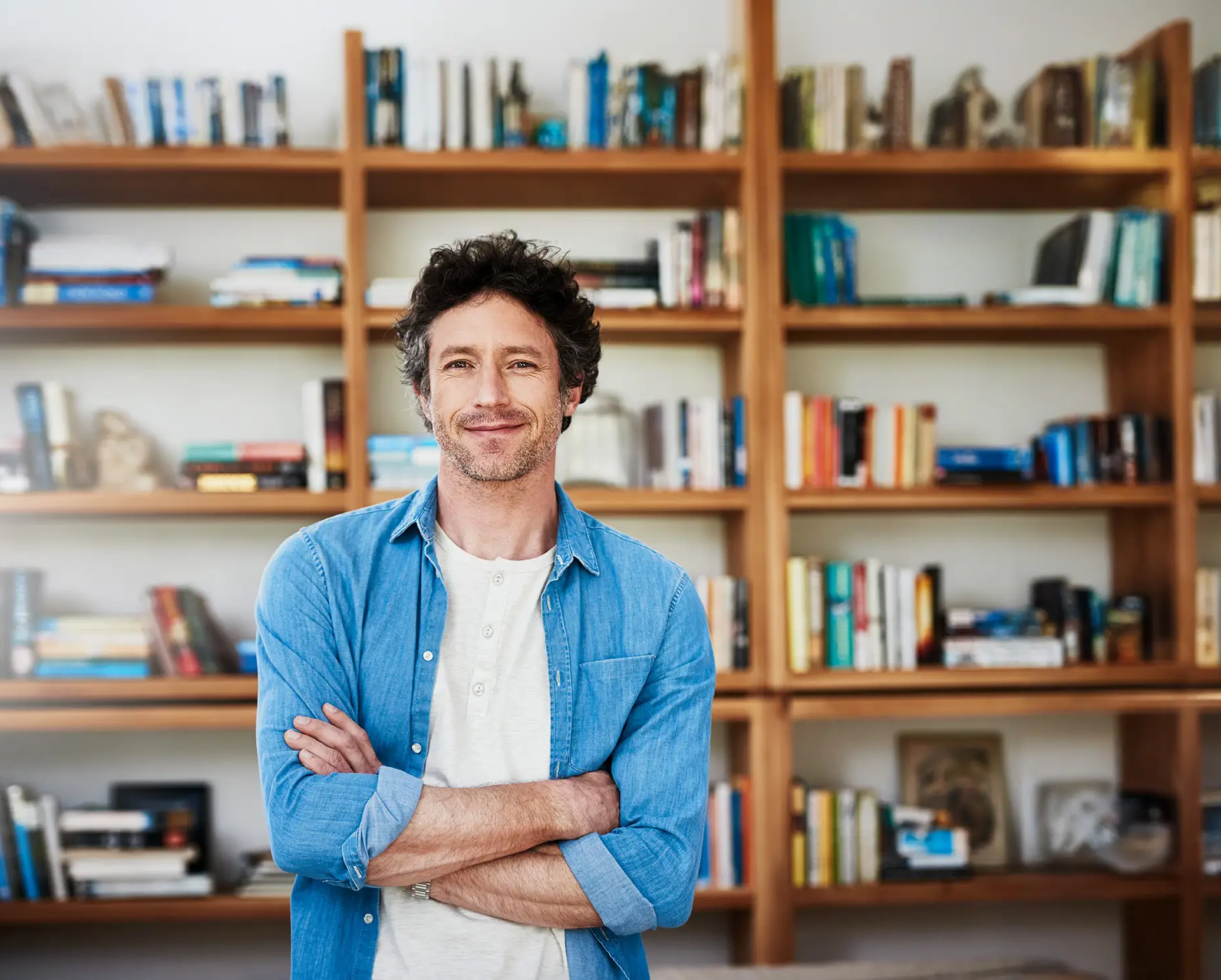 Mann schaut zuversichtlich in die Kamera. Hinter ihm ist ein wandhohes Regal voller Bücher.