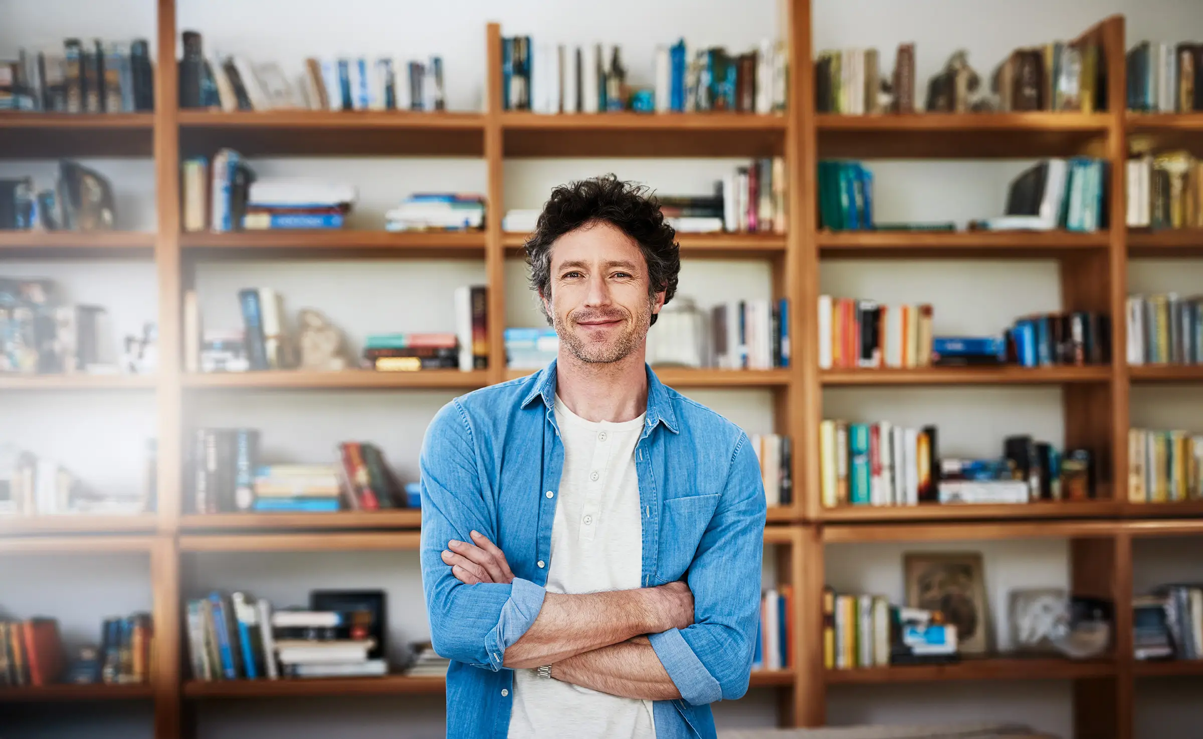 Mann schaut zuversichtlich in die Kamera. Hinter ihm ist ein wandhohes Regal voller Bücher.